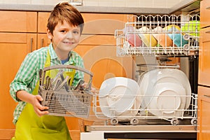 Happy boy pulling out cutlery of the dishwasher