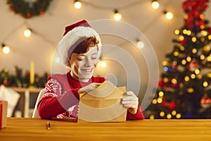 Happy boy putting his letter and wish list in an envelope before sending it to Santa