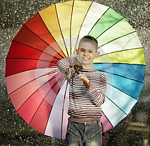 Happy boy with a rainbow umbrella in park