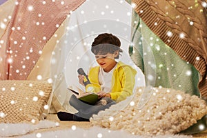 Happy boy reading book in kids tent at home