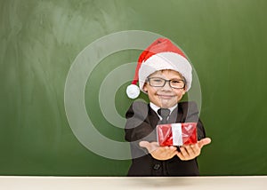 Happy boy in red christmas hat with gift near empty green blackboard