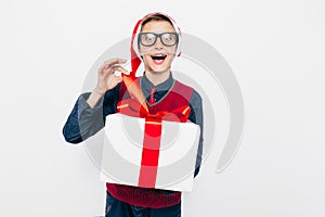 Happy boy in a red Santa hat. Stylish boy with Christmas gift, joyfully opens Christmas gift, on white background