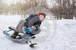 Happy boy rides a snow scooter from a mountain in the snow in winter