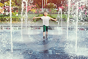 Happy boy running between water jets in city fountain. Summer vacation