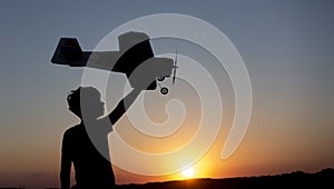 Happy Boy runs with a toy airplane on a field in the sunset light. Children play toy airplane. teenager dreams of flying and