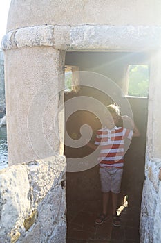 happy boy salutes and presents himself as middle-aged warrior in  guard loophole on fortress wall of ancient city