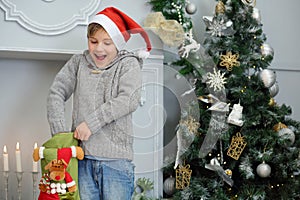 Happy boy in santa cap takes out sock gift near photo