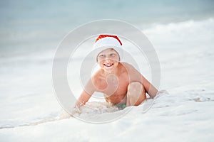 Happy boy in Santa`s hat swims on ocean surfline. Christamas and