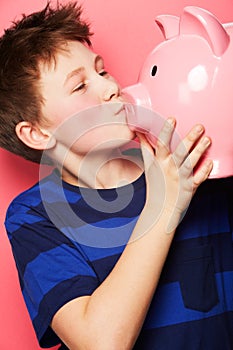 Happy boy, savings and kiss on piggy bank for investment, money or coins against a pink background. Little child or kid