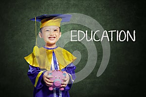 Happy boy with scholar gown and piggy bank