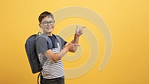 Happy boy schooler pointing at copy space, isolated on yellow