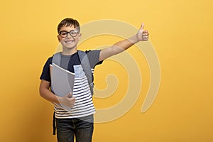 Happy boy schooler showing thumb up, isolated on yellow