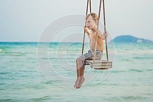 Happy boy sit on swing at the sea shore on sunset