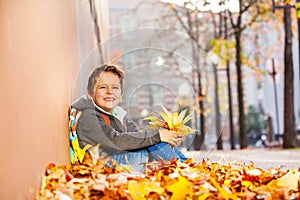 Happy boy sitting in leaf pile with rucksack