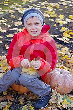 Happy boy sitting on pumpkin outdoors in autumn. Helloween.