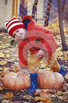 Happy boy sitting on pumpkin outdoors in autumn. Helloween.