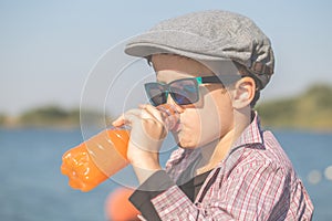 Happy boy sitting by the river and drinking juice