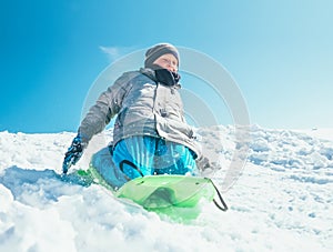 Happy boy slides down from snow hill using the sledge. Winter outdoor activity