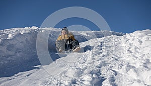 Happy boy sliding down snow hill on sled outdoors in winter, sledging and season concept