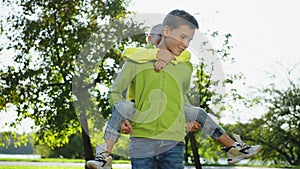 Happy boy spinning around with brother on shoulders in sunny park.