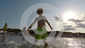 Happy boy splashes sea water at camera. Child body tempering at summer holidays.