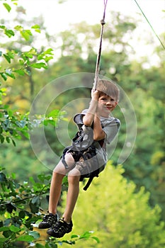 Happy boy successfully passed the obstacle course in the rope park and is flying in the air on the zip line among greenery and lus