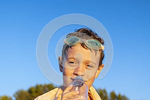 happy boy in swimming glasses drinks water from a bottle on the beach