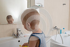 Happy boy taking bath in kitchen sink. Child playing with foam and soap bubbles in sunny bathroom with window. Little baby bathing