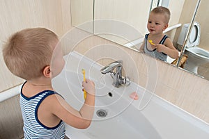 Happy boy taking bath in kitchen sink. Child playing with foam and soap bubbles in sunny bathroom with window. Little baby bathing