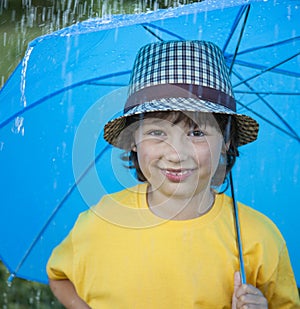 Happy boy with umbrella outdoors, child with an umbrella walks in rain