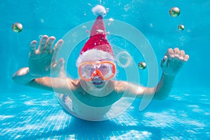 Happy boy on vacation dive in Santa hat underwater