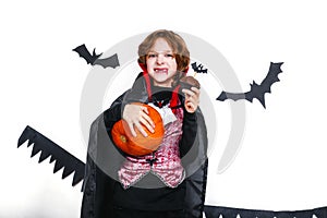 Happy boy in a vampire costume holding a pumpkin