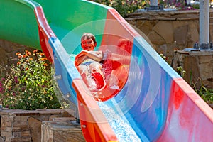 A happy boy on water slide in a swimming pool having fun during summer vacation in a beautiful aqua park. A boy