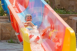 A happy boy on water slide in a swimming pool having fun during summer vacation in a beautiful aqua park. A boy