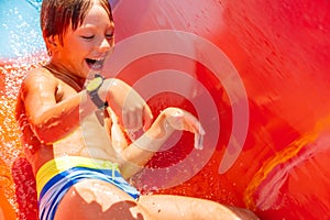 A happy boy on water slide in a swimming pool having fun during summer vacation in a beautiful aqua park. A boy