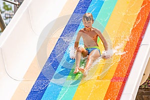 A happy boy on water slide in a swimming pool having fun during summer vacation in a beautiful aqua park. A boy