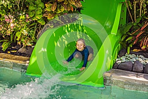 Happy boy on water slide in a swimming pool having fun during summer vacation in a beautiful tropical resort