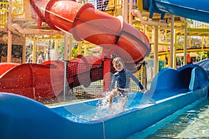 Happy boy on water slide in a swimming pool having fun during summer vacation in a beautiful tropical resort