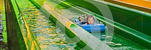 Happy boy on water slide in a swimming pool having fun during summer vacation in a beautiful tropical resort BANNER