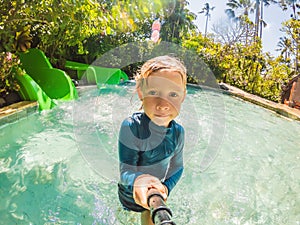 Happy boy on water slide in a swimming pool having fun during summer vacation in a beautiful tropical resort