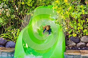 Happy boy on water slide in a swimming pool having fun during summer vacation in a beautiful tropical resort