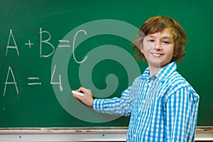 Happy boy writing on blackboard background. Educational and school concept