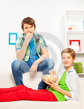 Happy boys eat popcorn while sitting on white sofa