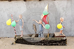 Happy boys play pirates and seafarers. Three brothers have fun together. The old boat is decorated with balloons