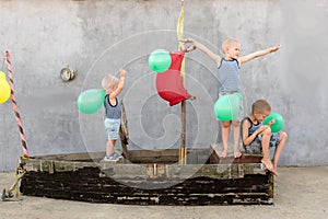 Happy boys play pirates and seafarers. Three brothers have fun together. The old boat is decorated with balloons