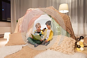 Happy boys reading book in kids tent at home