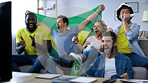 Happy Brazilian friends watching match at home celebrating goal of football team