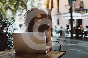 Happy Brazilian girl freelancer with laptop in street cafe