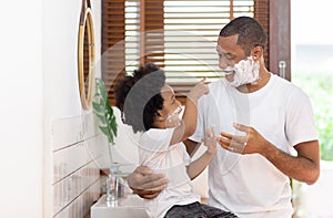 Happy Brazilian Single Father and little son having fun with shaving foam on their faces in bathroom at home together