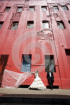 Happy bridal couple standing on sidewalk below tall red building